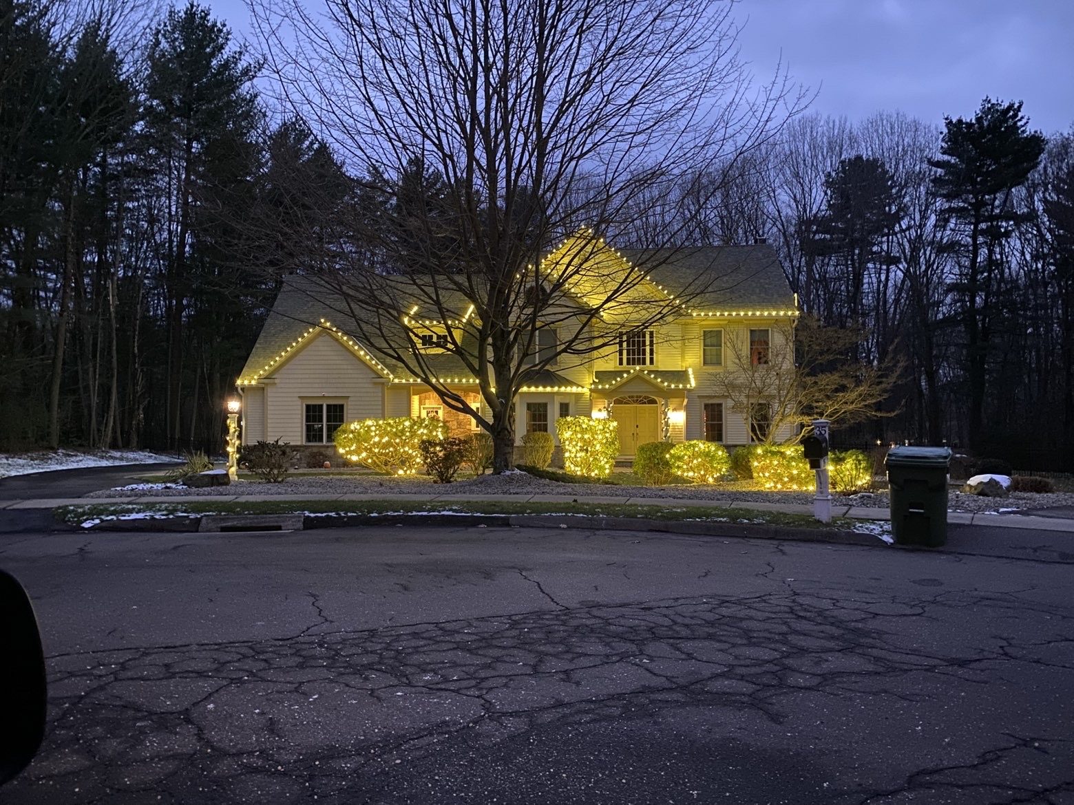 Colonial home at dusk with lit rooflines and glowing netted shrubs