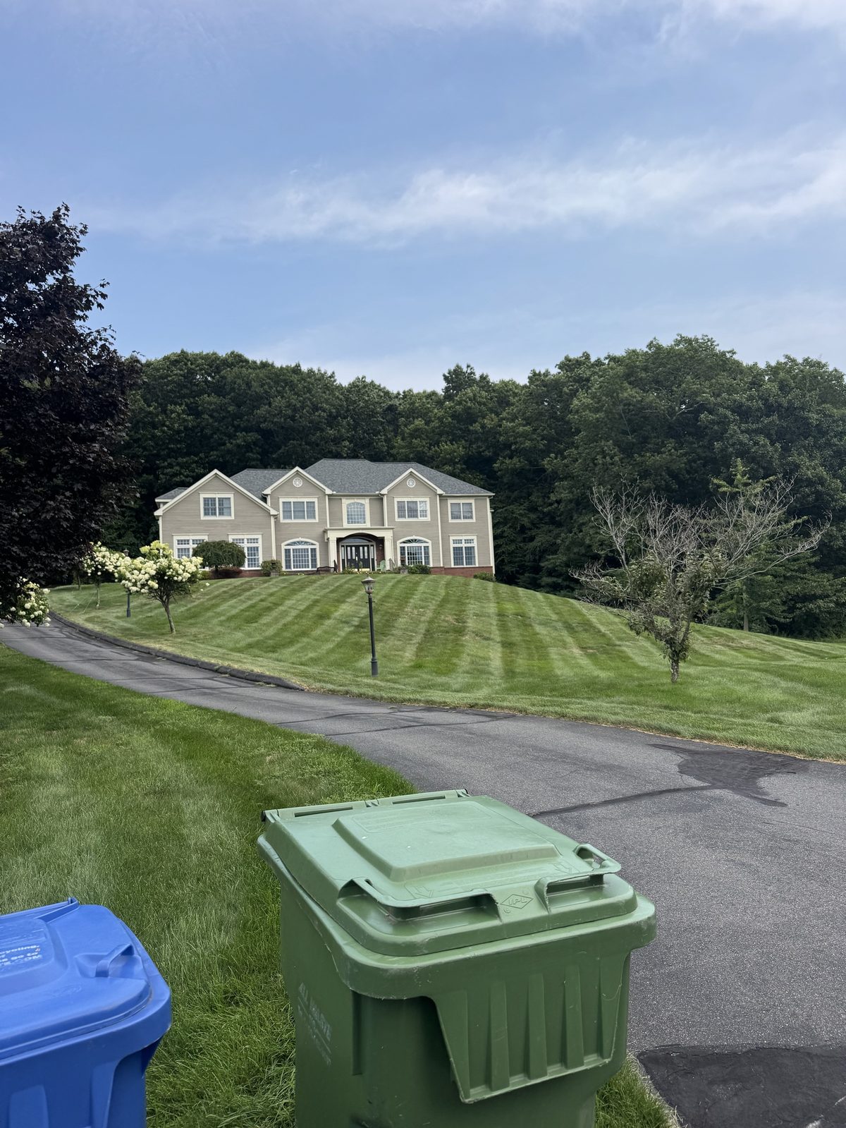 Striped lawn running up a hill to a large Colonial home