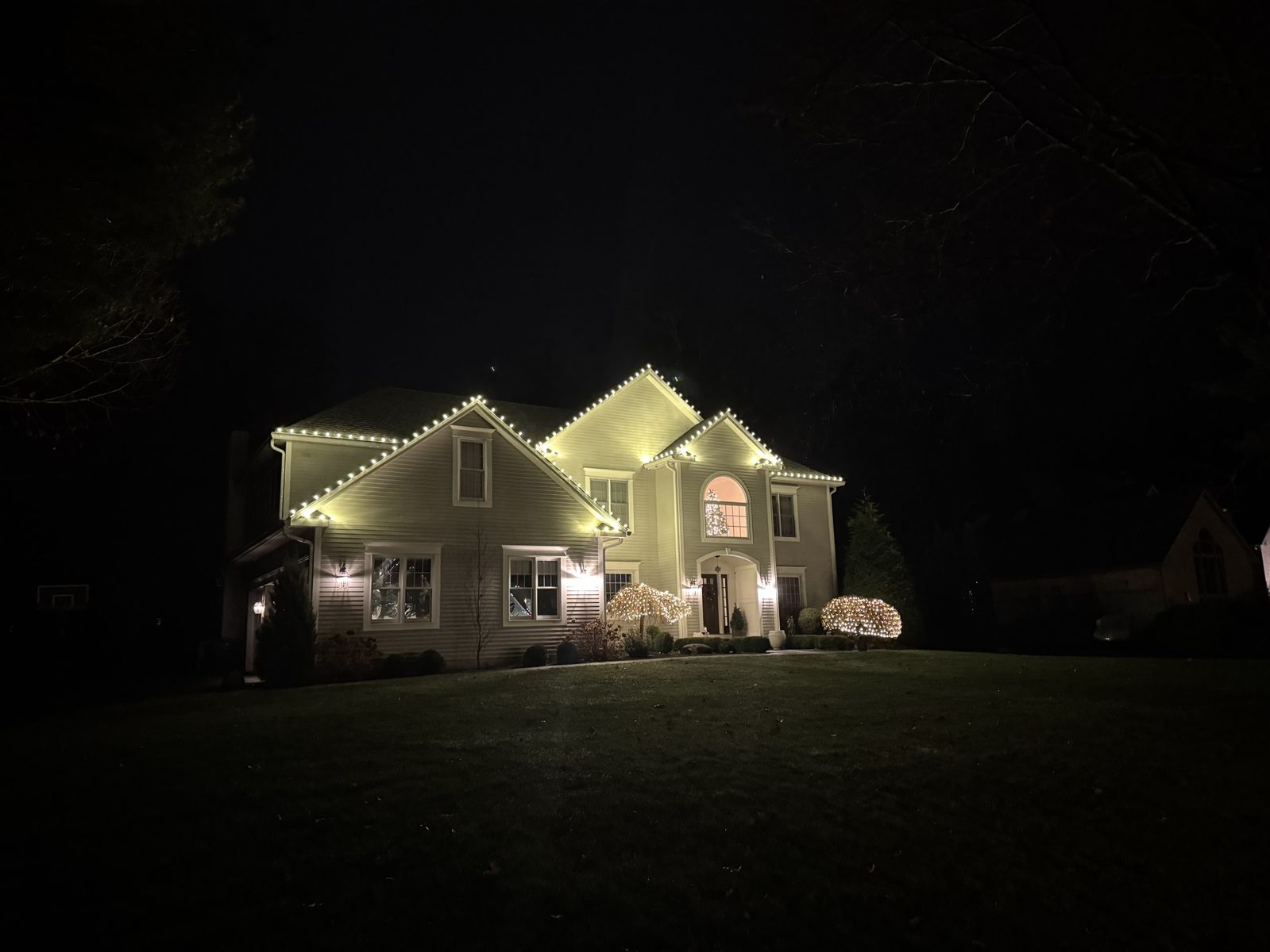Two-story home with roofline lights and lit ornamental shrubs