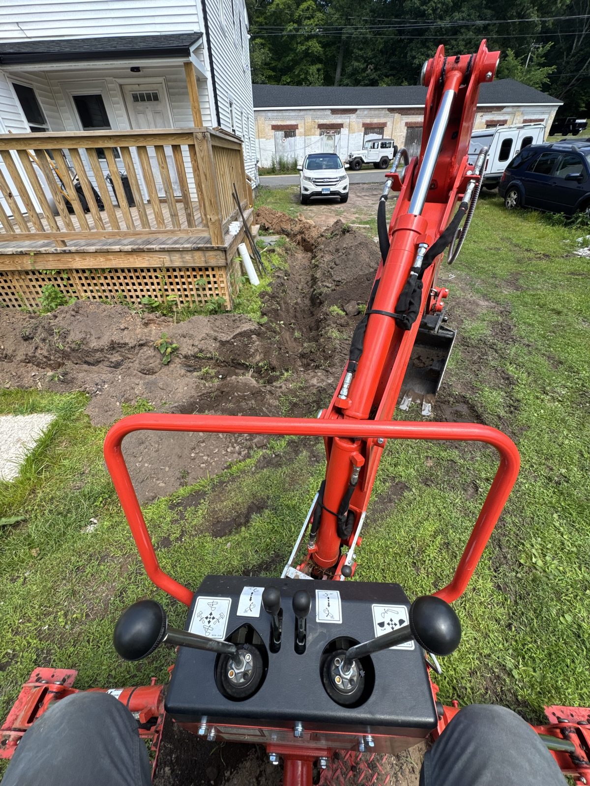 Mini excavator digging a drainage line beside a house