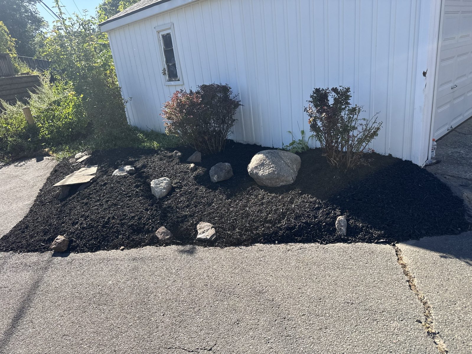 Finished black mulch bed with boulders and shrubs beside a garage