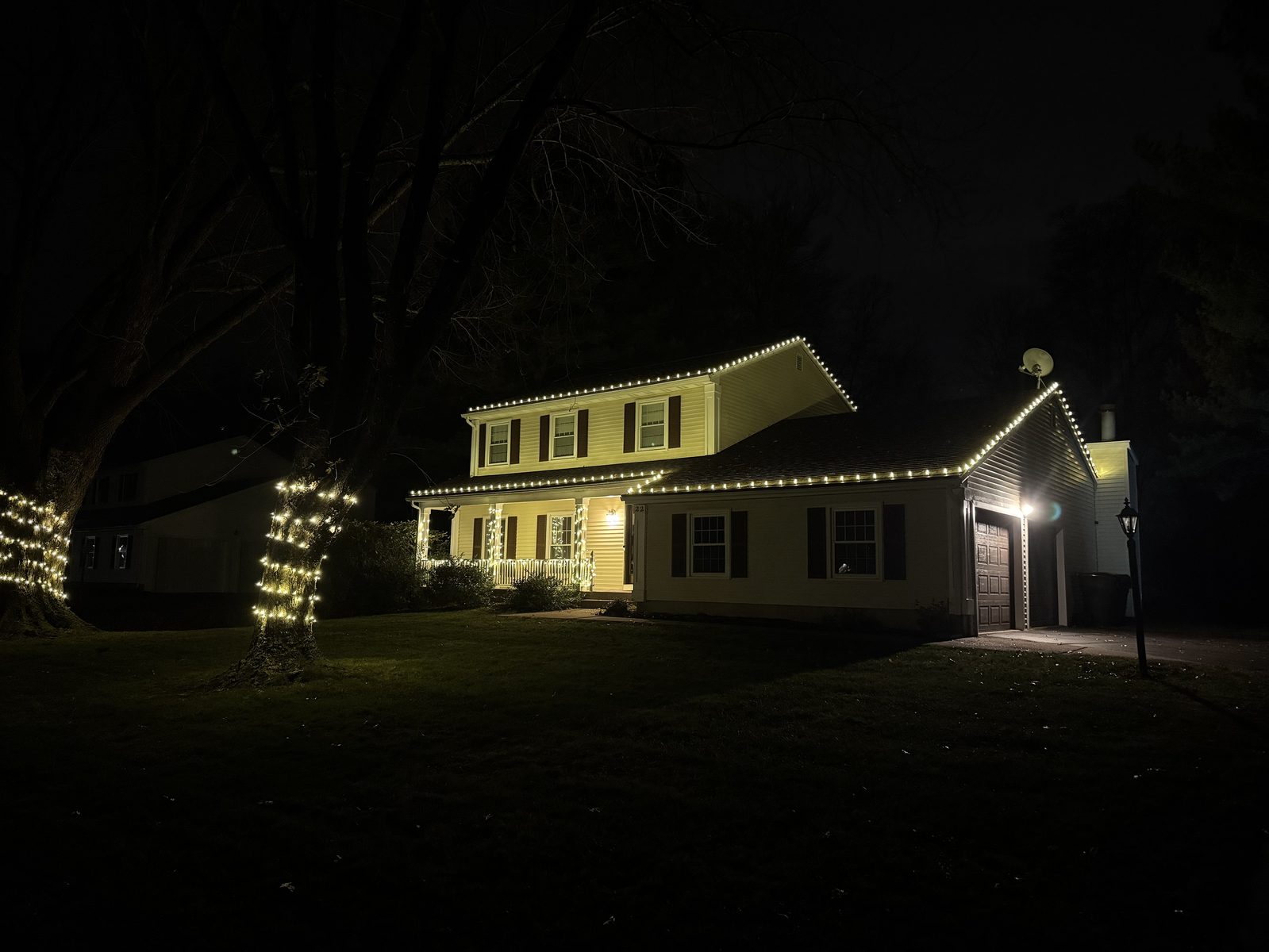 Colonial home with roofline C9 lights and wrapped tree trunks at night
