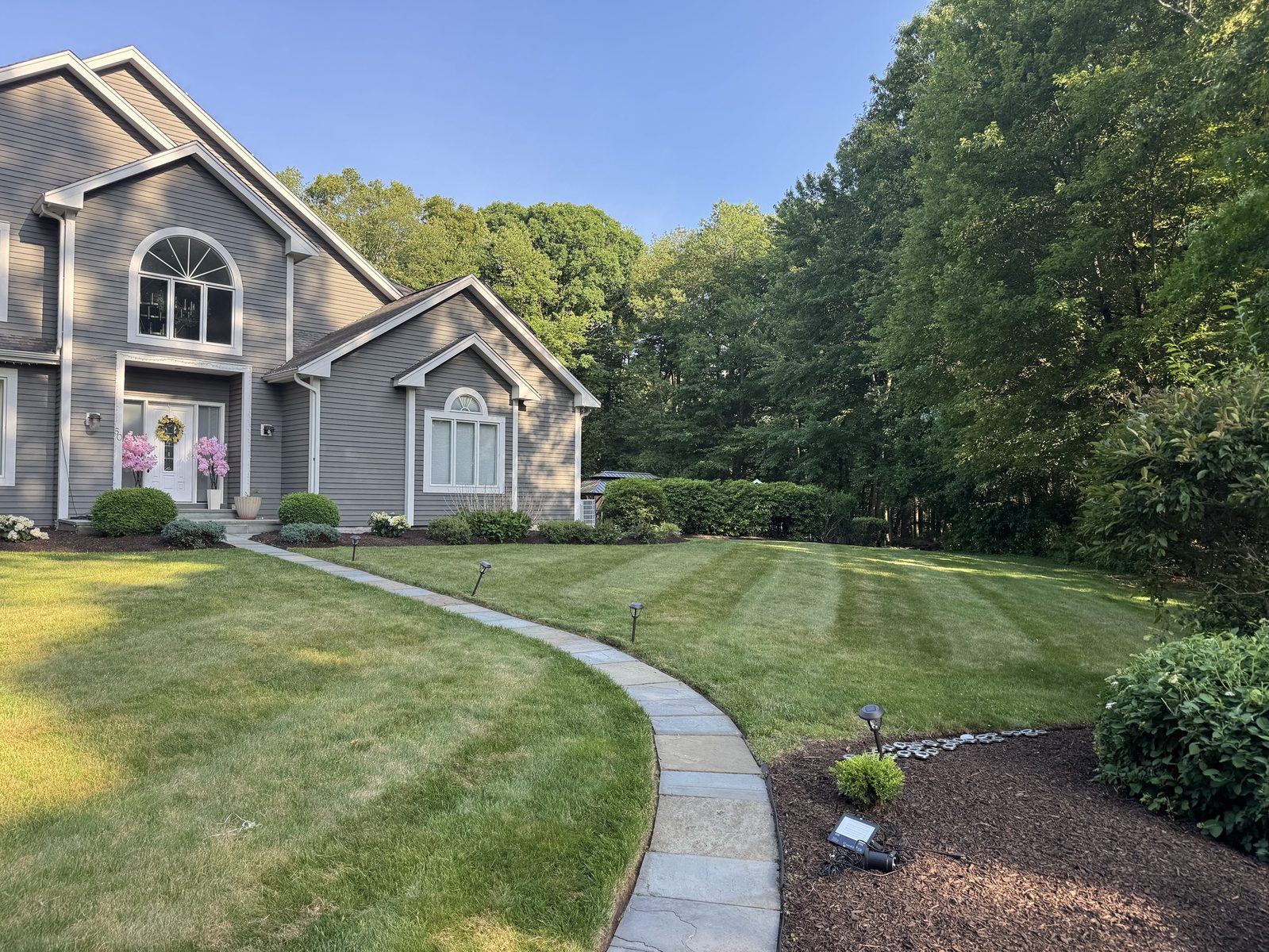 Striped front lawn with a curved stone walkway and landscape lights